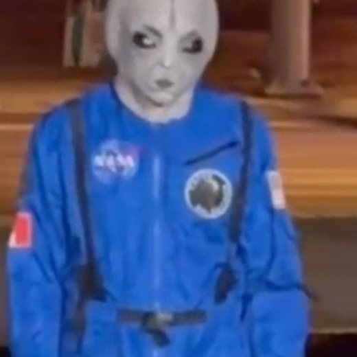 One of their crew in an alien mask and a blue flight suit, at night