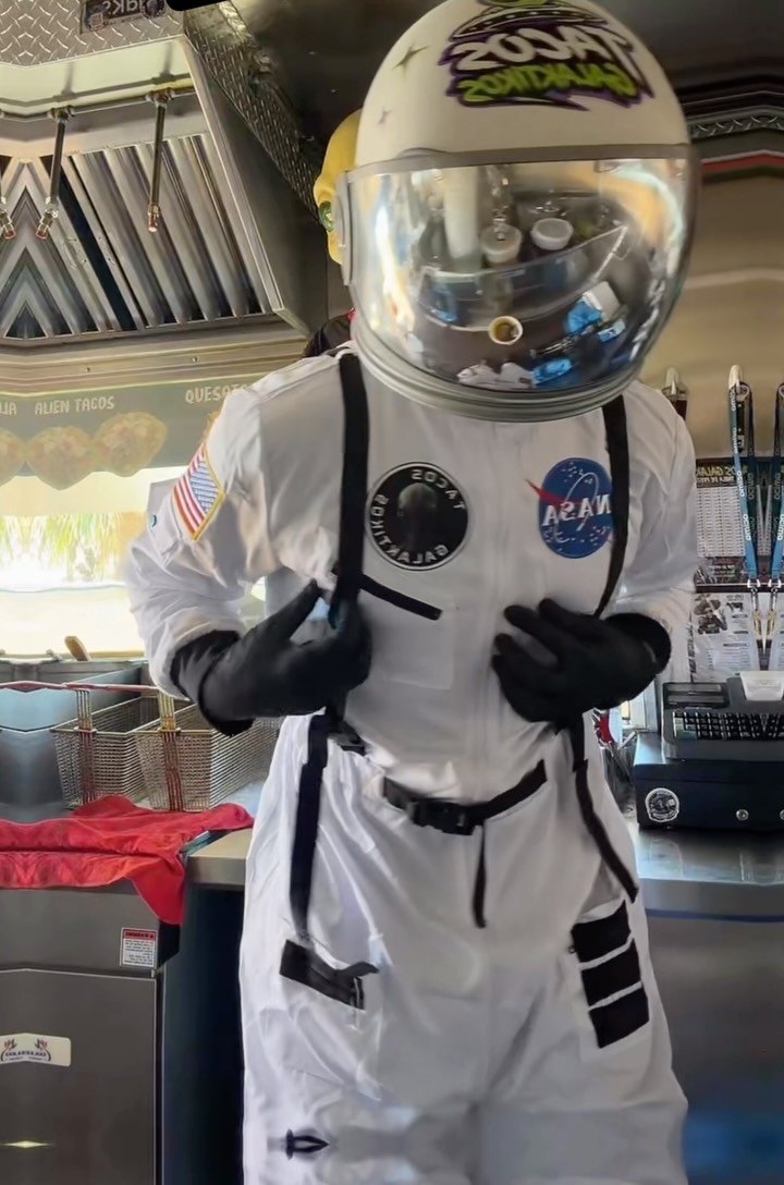 One of their crew in a full white astronaut suit and mirrored helmet, inside the truck