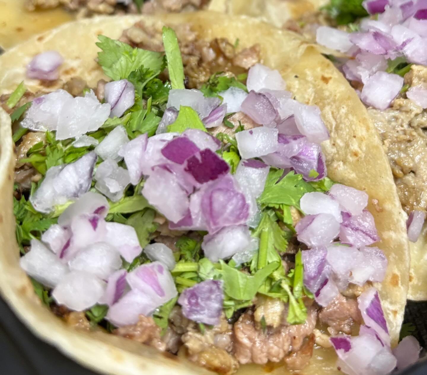 Flour-tortilla tacos close up, the meat piled with chopped white onion and cilantro, from their Instagram